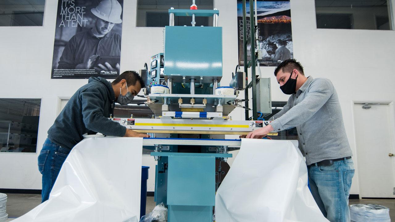 Two team members working on large grey welding machine